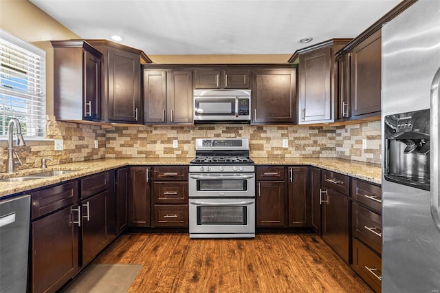 kitchen featuring tasteful backsplash, dark brown cabinets, dark wood finished floors, stainless steel appliances, and a sink