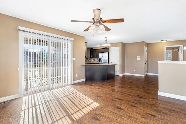 unfurnished living room with dark wood finished floors, ceiling fan with notable chandelier, visible vents, and baseboards