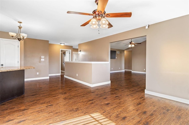 spare room featuring baseboards, wood finished floors, and ceiling fan with notable chandelier