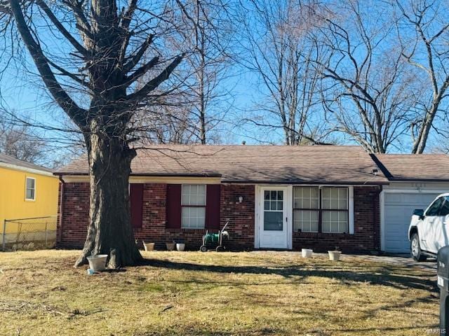 ranch-style home with a front lawn, fence, roof with shingles, an attached garage, and brick siding