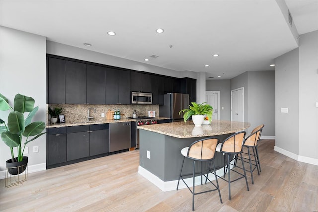 kitchen with stainless steel appliances, tasteful backsplash, an island with sink, light wood finished floors, and baseboards