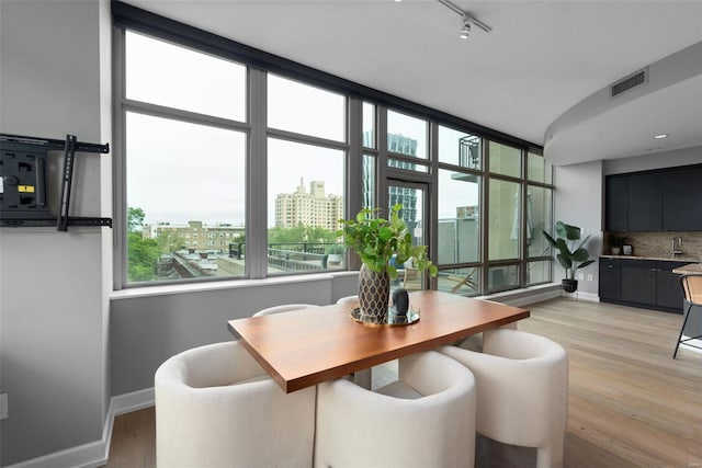 dining room with track lighting, visible vents, light wood finished floors, a city view, and baseboards