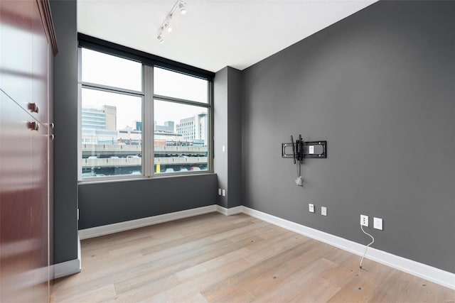 unfurnished room with light wood finished floors, a city view, baseboards, and track lighting
