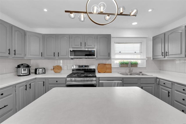 kitchen featuring gray cabinets, a sink, stainless steel appliances, light countertops, and tasteful backsplash