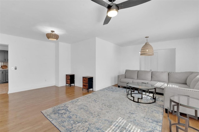 living room with ceiling fan, baseboards, and light wood-style flooring