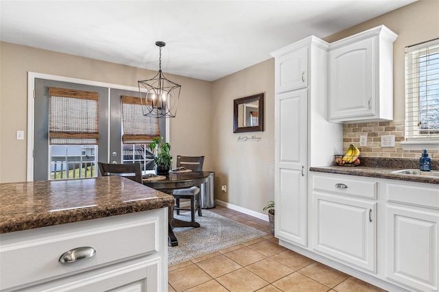 kitchen with dark countertops, a chandelier, white cabinets, and tasteful backsplash