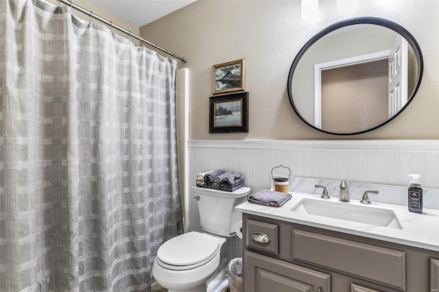 full bathroom featuring a shower with shower curtain, vanity, toilet, and wainscoting