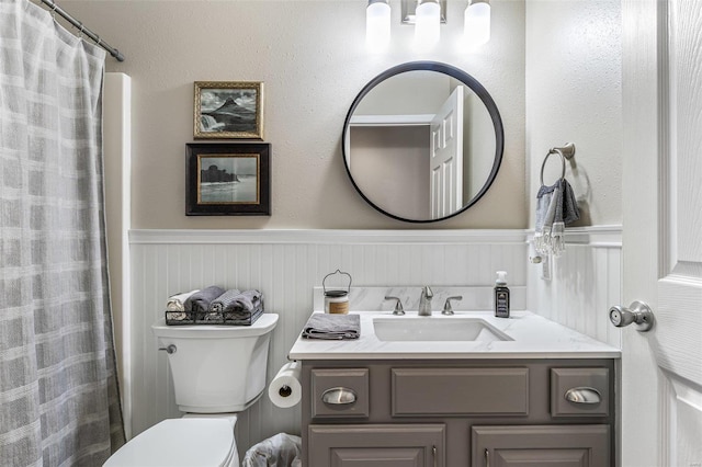 bathroom featuring a wainscoted wall, toilet, and vanity