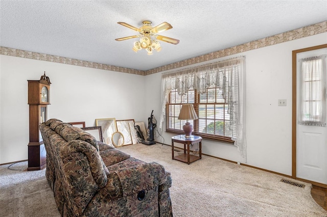 living area with carpet flooring, a ceiling fan, baseboards, and a textured ceiling