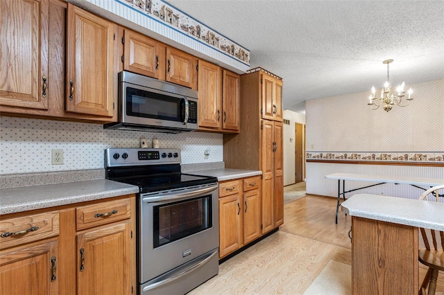 kitchen featuring light wood finished floors, stainless steel appliances, a textured ceiling, brown cabinets, and a chandelier