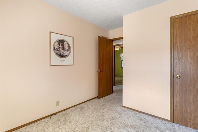 unfurnished bedroom featuring light colored carpet, a textured ceiling, and baseboards