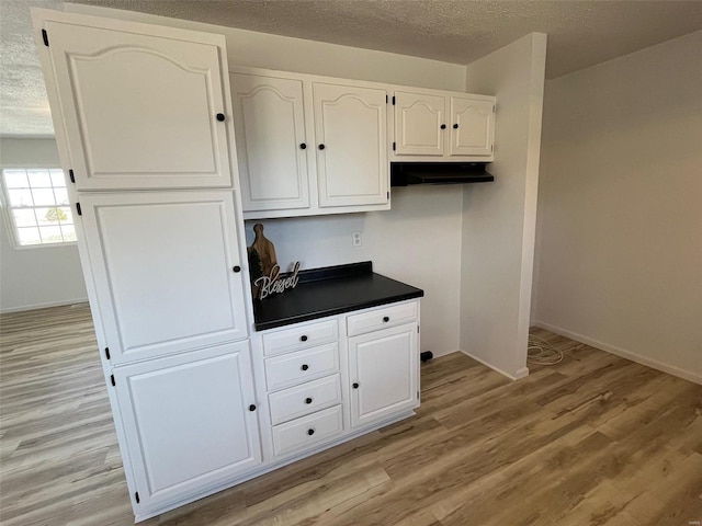 kitchen featuring a textured ceiling, dark countertops, white cabinets, and light wood finished floors