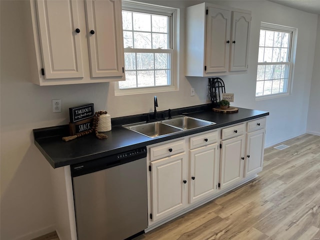 kitchen featuring dark countertops, dishwasher, light wood-style flooring, white cabinets, and a sink