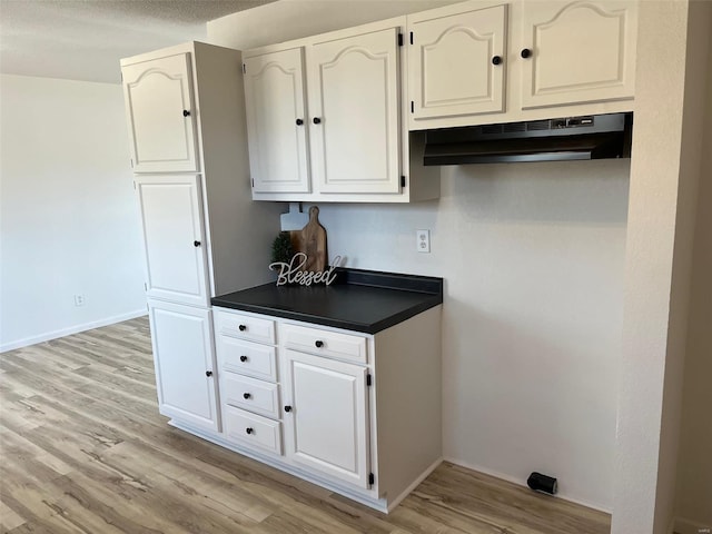 kitchen featuring white cabinetry, dark countertops, light wood-type flooring, and under cabinet range hood