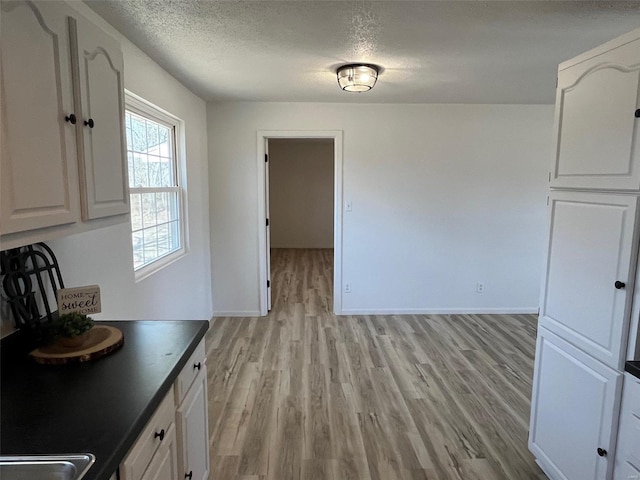 kitchen featuring light wood finished floors, dark countertops, white cabinetry, baseboards, and a textured ceiling