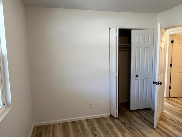 unfurnished bedroom with a closet, baseboards, and light wood-style floors