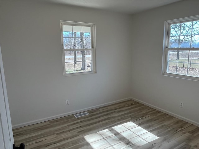 spare room with wood finished floors, visible vents, and baseboards