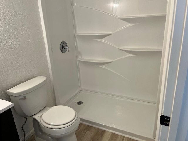 full bath featuring toilet, wood finished floors, a textured wall, and a shower