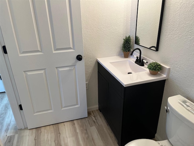 bathroom featuring toilet, wood finished floors, vanity, and a textured wall