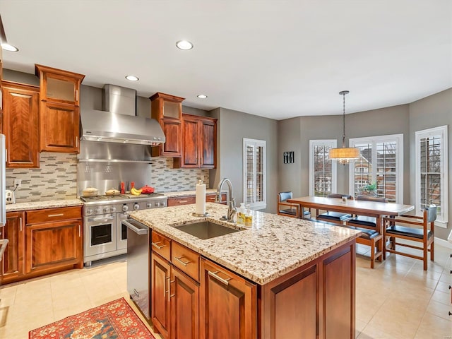 kitchen featuring tasteful backsplash, a sink, wall chimney range hood, stainless steel appliances, and a kitchen island with sink