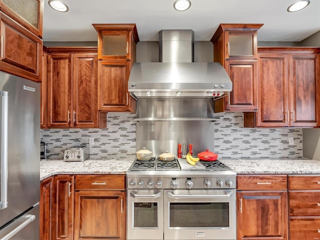 kitchen featuring light stone counters, backsplash, appliances with stainless steel finishes, and wall chimney range hood