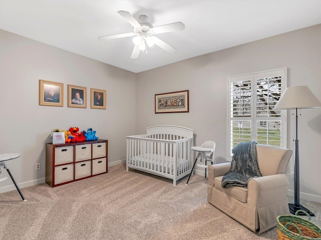 carpeted bedroom with baseboards, a nursery area, and a ceiling fan