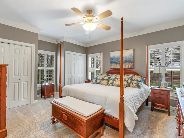 carpeted bedroom featuring baseboards, two closets, ornamental molding, and a ceiling fan