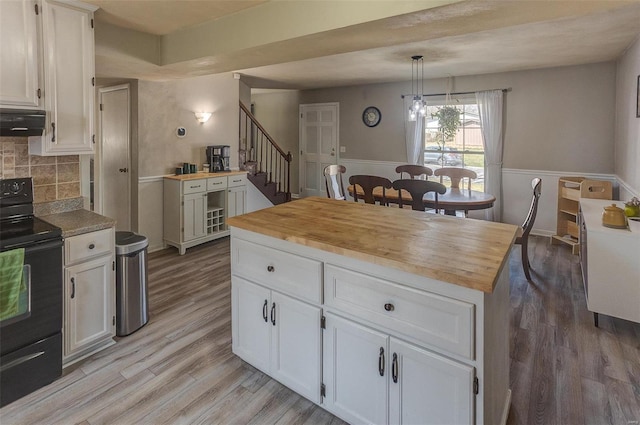 kitchen with range hood, black / electric stove, light wood-type flooring, and butcher block countertops