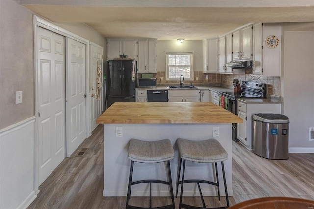 kitchen featuring wood finished floors, a sink, black appliances, under cabinet range hood, and wood counters