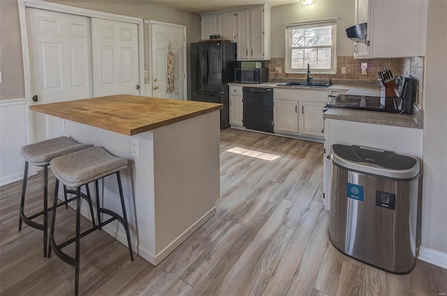 kitchen featuring black appliances, butcher block countertops, a sink, light wood-style floors, and decorative backsplash