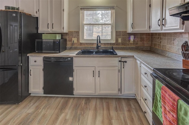 kitchen featuring black appliances, a sink, ventilation hood, white cabinets, and light wood finished floors