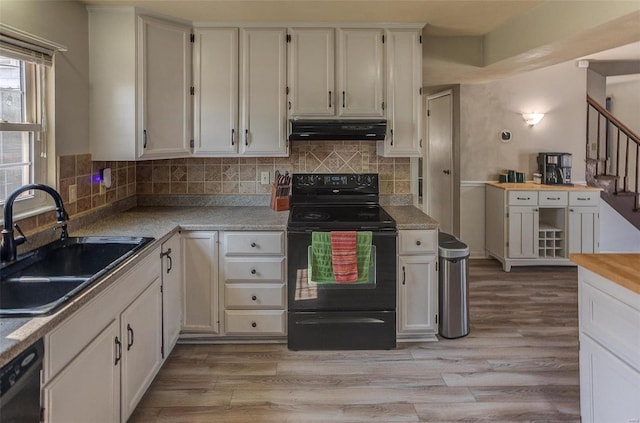 kitchen featuring under cabinet range hood, black appliances, light wood-type flooring, and a sink