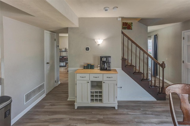 bar featuring visible vents, stairs, baseboards, and dark wood-style flooring