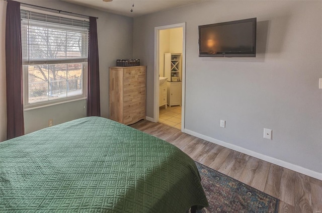 bedroom featuring baseboards, ensuite bath, and wood finished floors