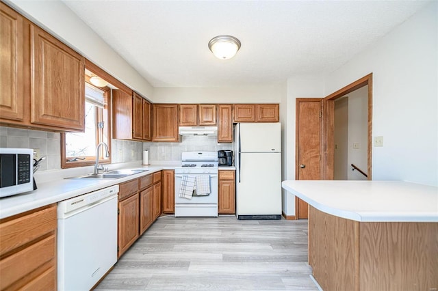 kitchen with decorative backsplash, white appliances, light wood finished floors, and a sink