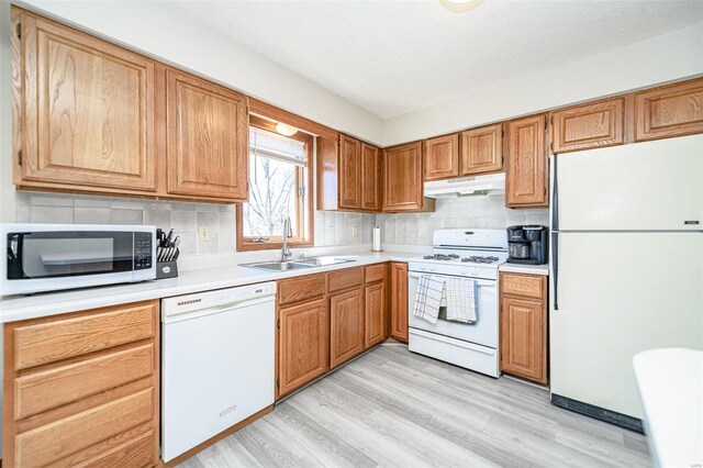 kitchen with light wood-type flooring, a sink, under cabinet range hood, white appliances, and light countertops