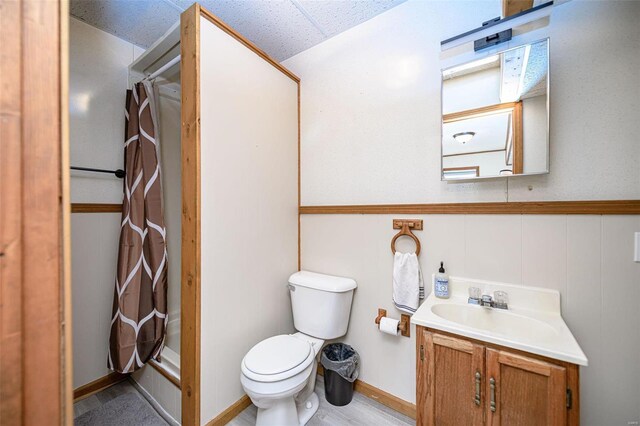 full bath featuring a wainscoted wall, a drop ceiling, toilet, a shower with curtain, and vanity