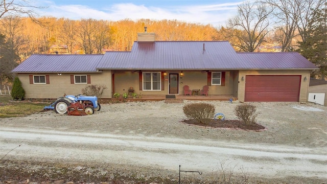 ranch-style house with driveway, covered porch, an attached garage, metal roof, and a chimney