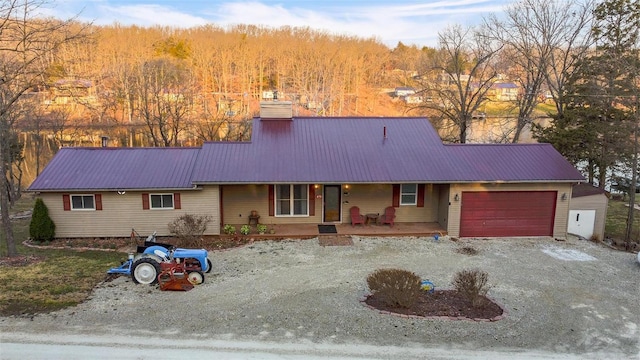 ranch-style house with a porch, an attached garage, driveway, and metal roof