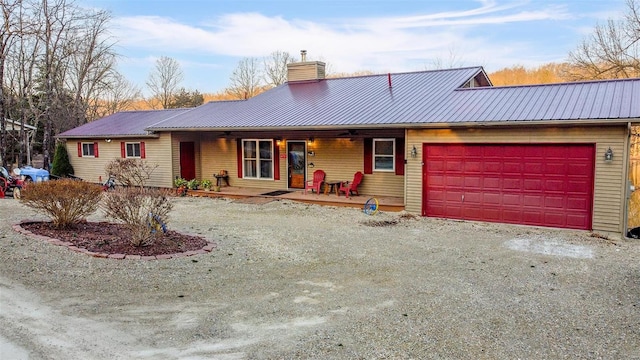 single story home featuring metal roof, a chimney, a garage, and dirt driveway