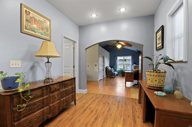 foyer with a ceiling fan, baseboards, arched walkways, vaulted ceiling, and light wood-type flooring