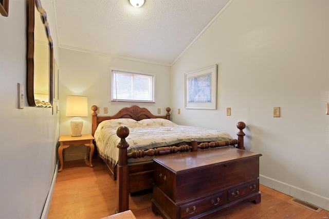 bedroom featuring baseboards, visible vents, light wood finished floors, ornamental molding, and vaulted ceiling