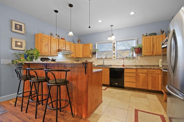 kitchen featuring backsplash, under cabinet range hood, a kitchen bar, appliances with stainless steel finishes, and a peninsula