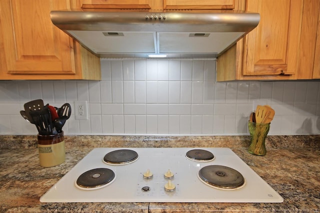 details featuring under cabinet range hood, tasteful backsplash, white electric cooktop, and dark stone counters