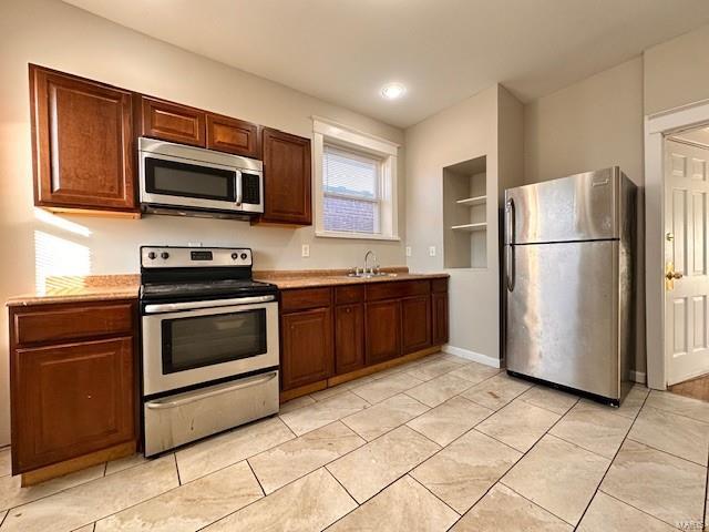 kitchen with a sink, stainless steel appliances, light tile patterned floors, and light countertops