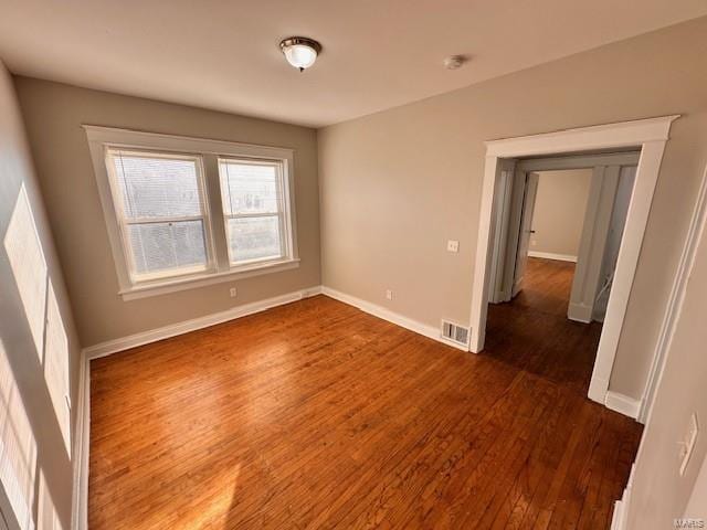 spare room featuring dark wood-style floors, visible vents, and baseboards