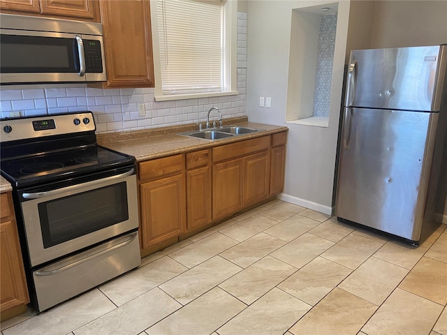 kitchen with brown cabinets, a sink, backsplash, appliances with stainless steel finishes, and light tile patterned floors