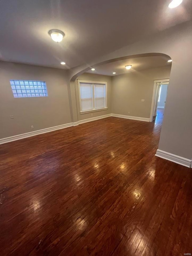 spare room with arched walkways, dark wood-style floors, and baseboards