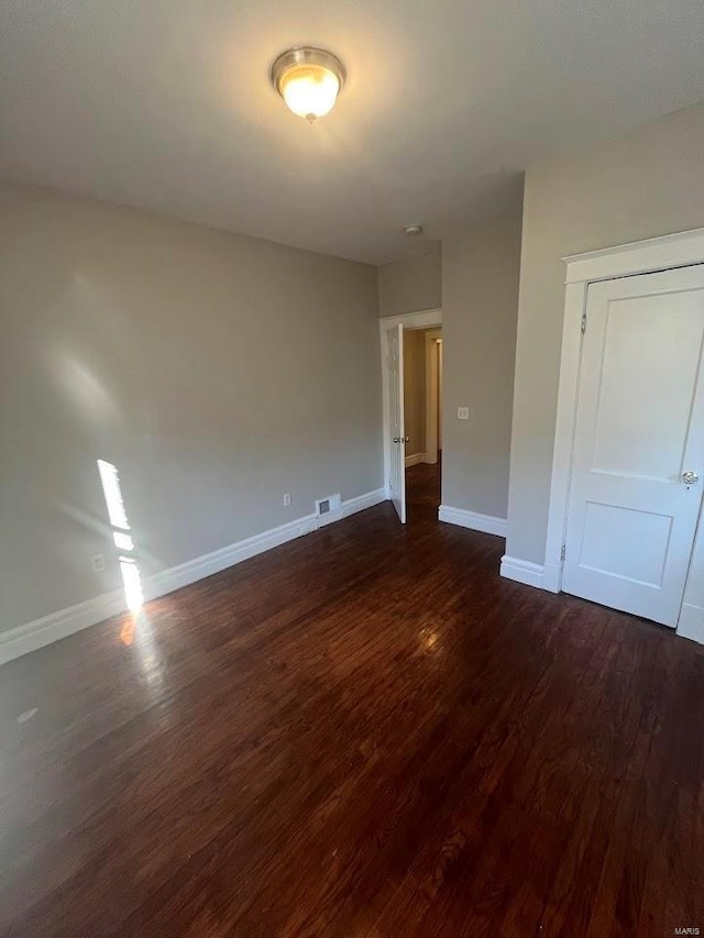 empty room featuring dark wood-type flooring, baseboards, and visible vents