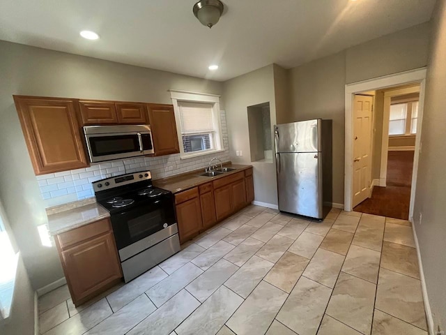 kitchen with baseboards, light countertops, decorative backsplash, stainless steel appliances, and a sink